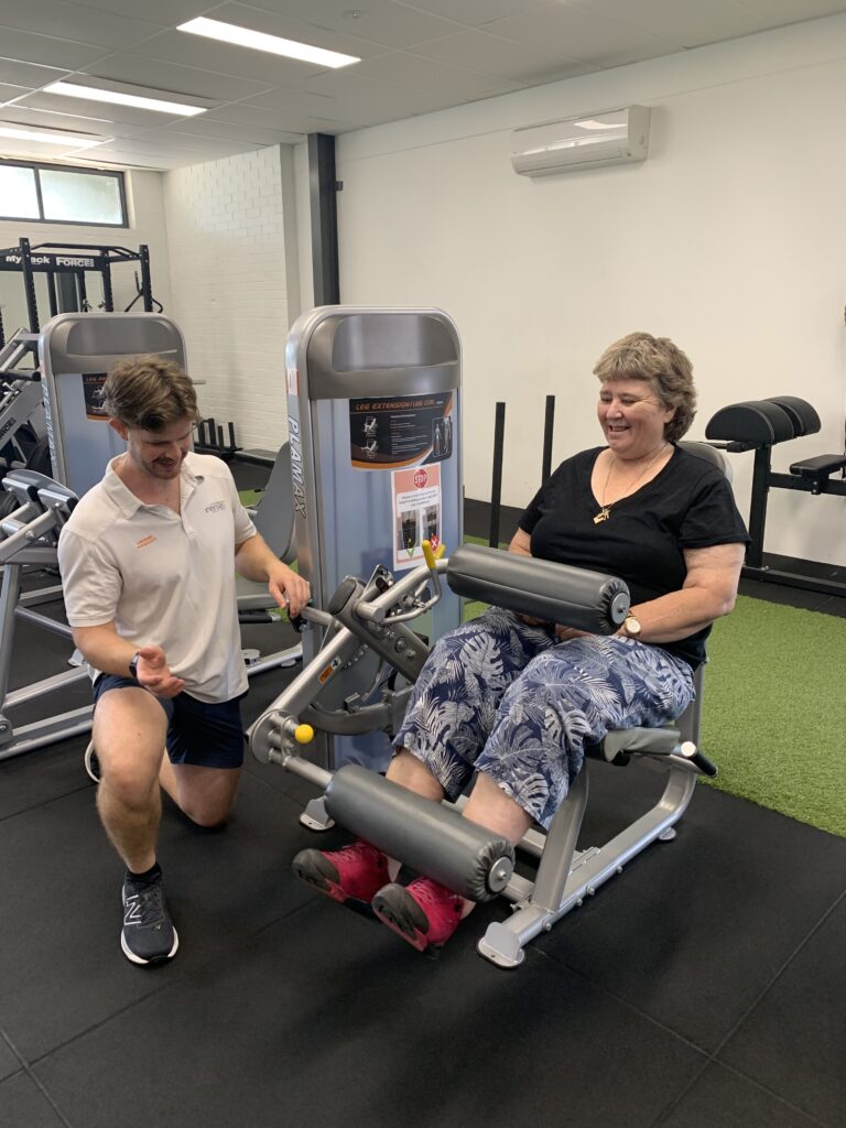 A woman performing leg exercises with resistance bands under the supervision of an exercise physiologist in a rehabilitation clinic