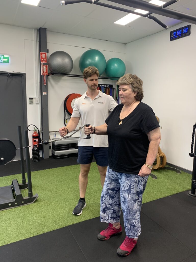 A woman performing strength exercises with dumbbells under the guidance of an exercise physiologist in a rehabilitation clinic
