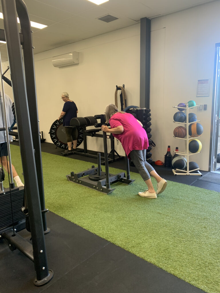A woman performing stretching exercises on an exercise mat under the guidance of an exercise physiologist in a rehabilitation clinic