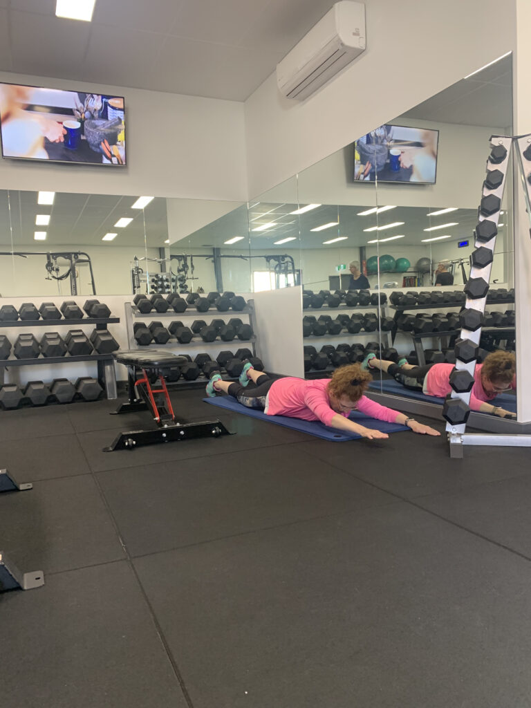 A woman practicing yoga on a mat with serene focus, guided by an exercise physiologist in a rehabilitation clinic