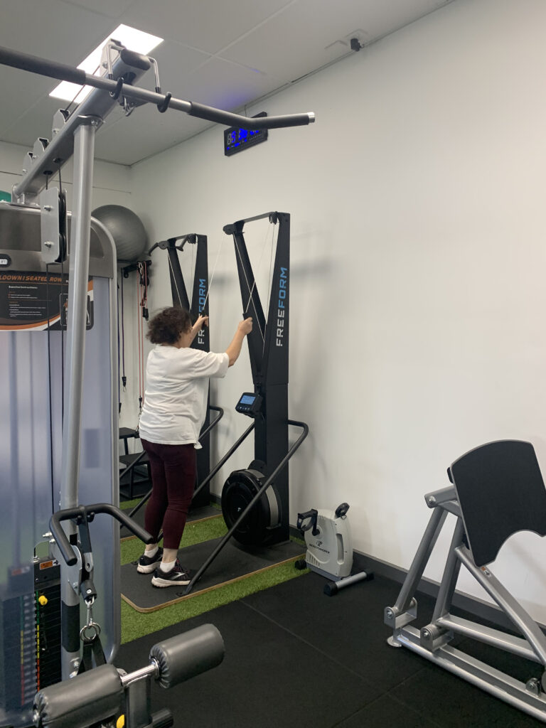 A woman using gym equipment under the supervision of an exercise physiologist in a rehabilitation clinic