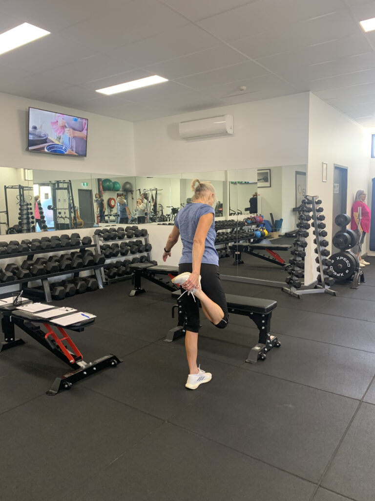 A woman stretching her legs in a gym under the guidance of an exercise physiologist