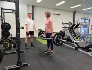 A woman in athletic attire lifting weights with proper form under the guidance of an exercise physiologist in a well-equipped gym