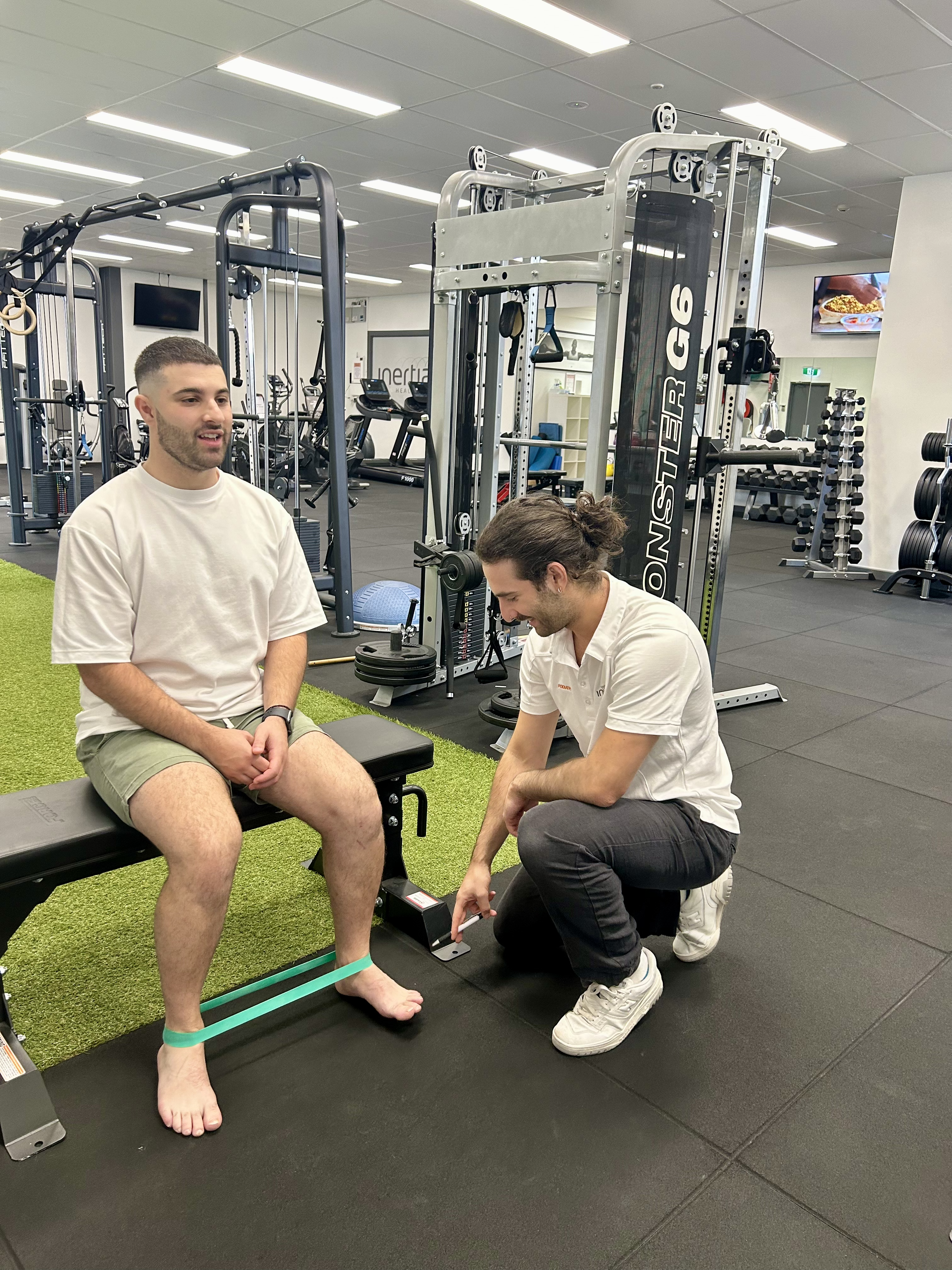 A man exercises his legs under the guidance of a podiatrist in a gym setting.