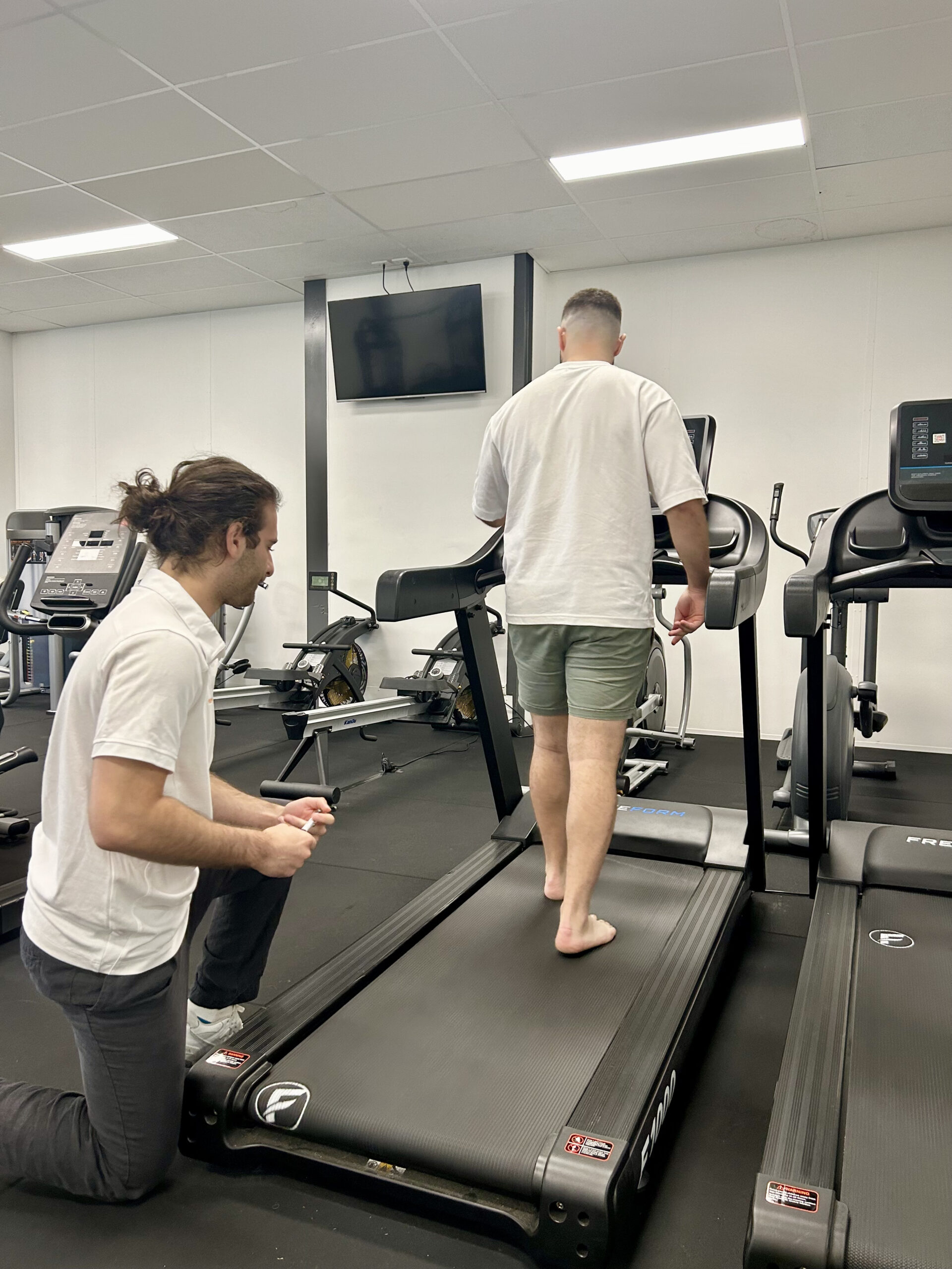 A podiatry patient walks on a treadmill during a gait analysis session, monitored by a podiatrist.