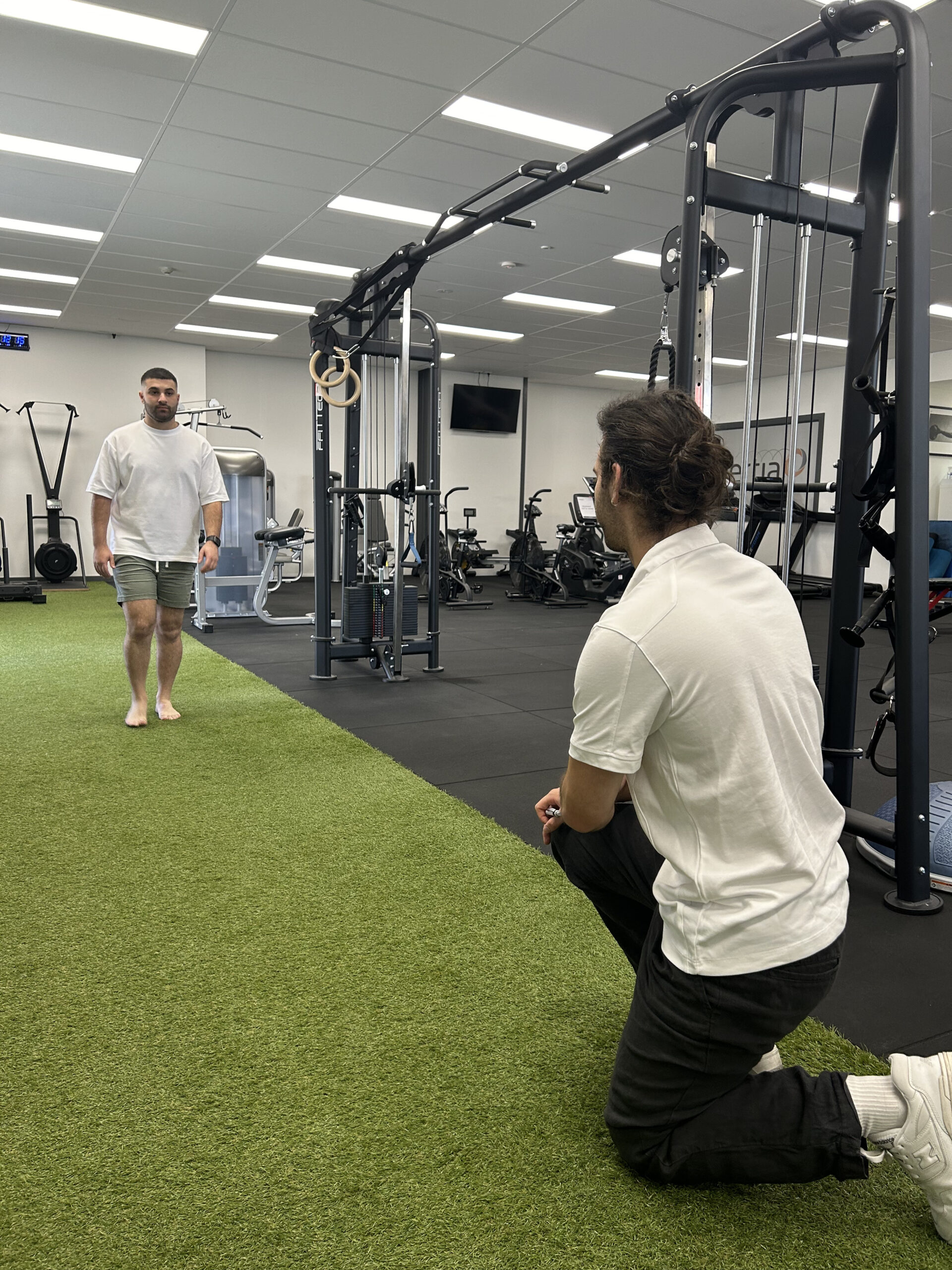A podiatry patient walks along a corridor during an assessment, observed by a podiatrist.