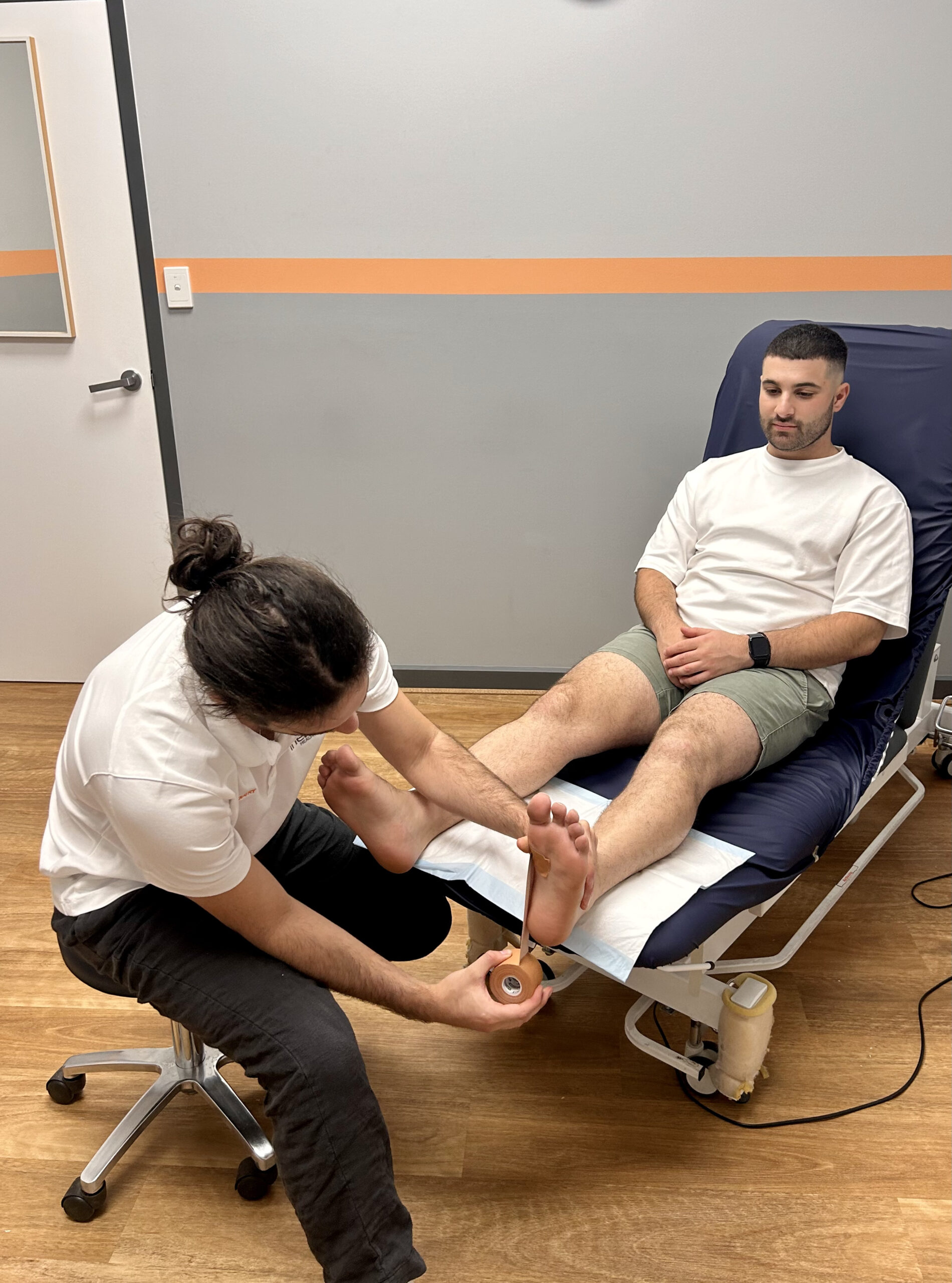 A podiatrist examines a seated podiatry patient's feet in a clinical setting.