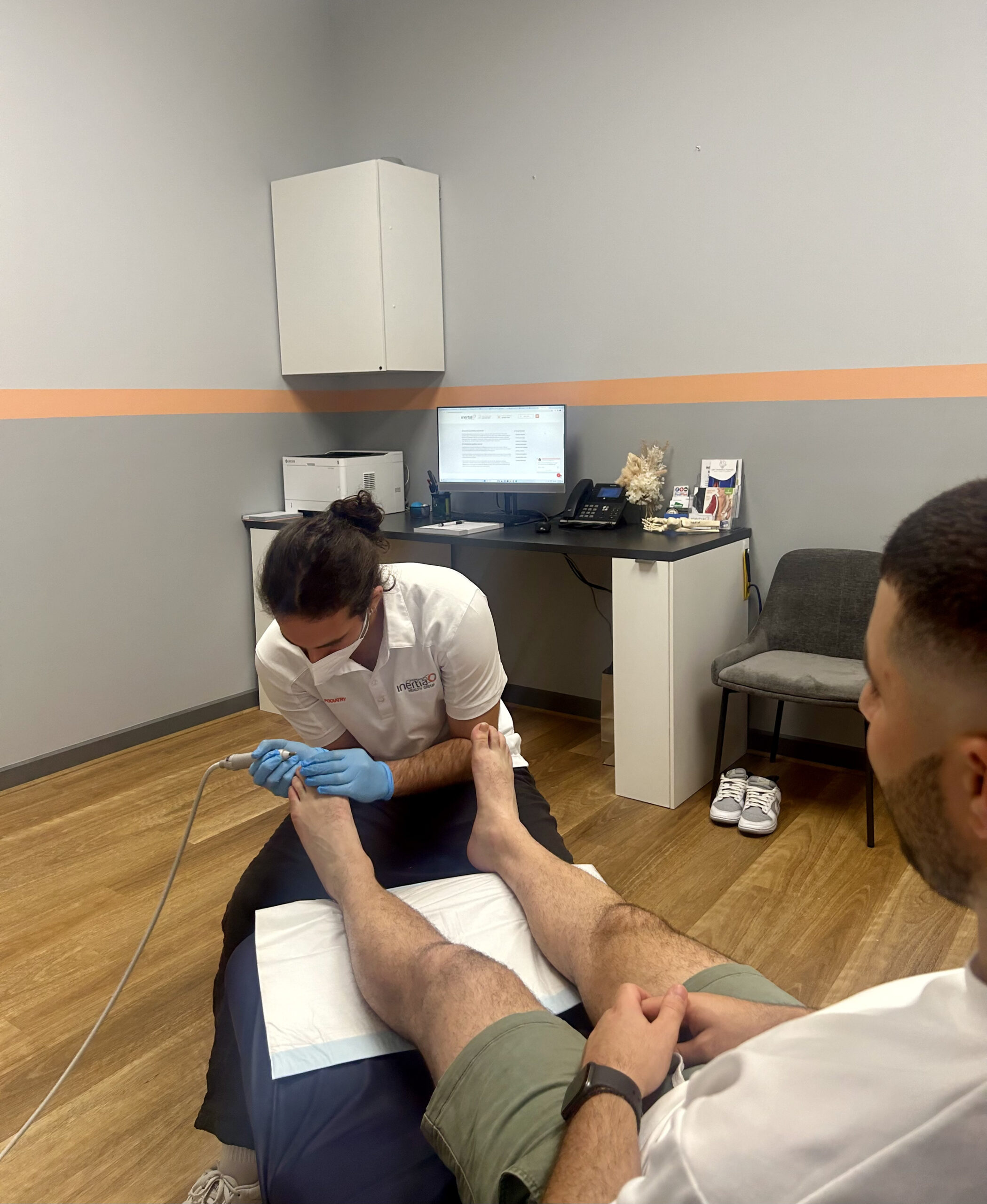 A podiatrist applies treatment to his patient's foot in a clinical setting at Inertia Health Group's Port Adelaide clinic